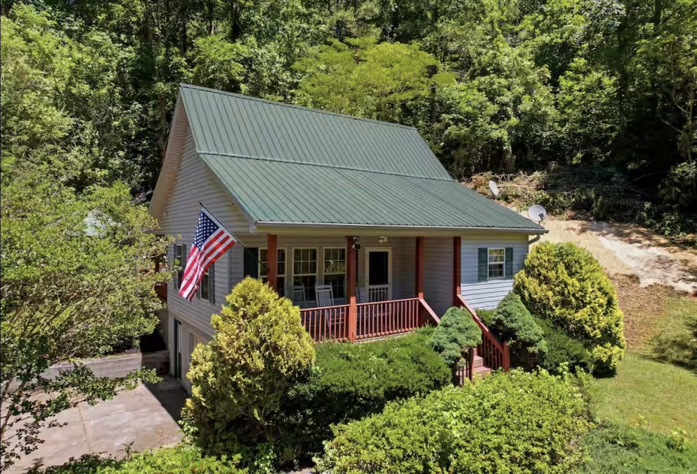 The cabin with its green metal roof, front porch and flag, set into the wooded hillside